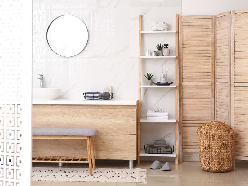 Freestanding bamboo ladder shelf styled in a small beige bathroom. Features rolled towels, skincare items, and a trailing plant — ideal for modern small bathrooms in apartments with minimalist or luxury design.