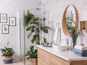 Small apartment bathroom with a cozy, plant-filled decor setup. Features include a white ceramic sink, wooden floating shelves, and low-maintenance indoor plants like spider plant, carnations, and purple flowers. Natural sunlight streams through an open window, enhancing the biophilic, modern aesthetic. Perfect inspiration for cozy small apartment bathroom decor ideas, modern small bathrooms with plants, and space-saving styling for renters.